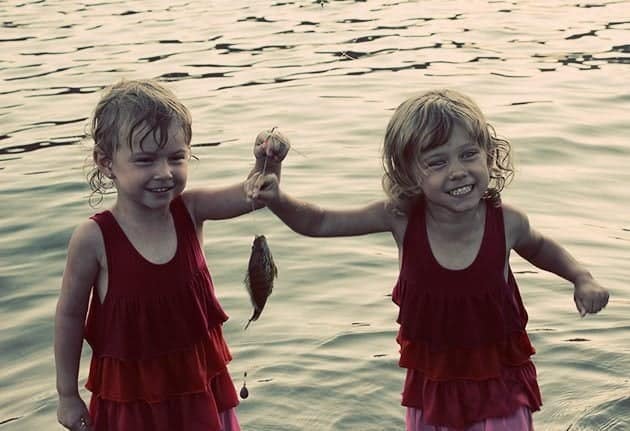 two kids wearing same red dress holding a string with a fish on it