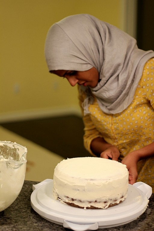 covering the two layer cake with vanilla frosting