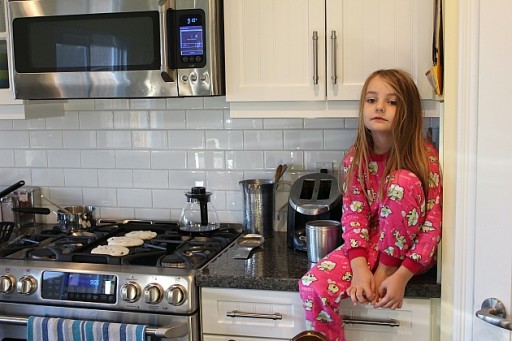 little girl in red sleeping pajamas sitting on top of the kitchen table