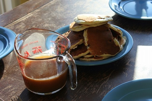 sugar syrup in a Pyrex measuring cup and pancakes in a blue plate