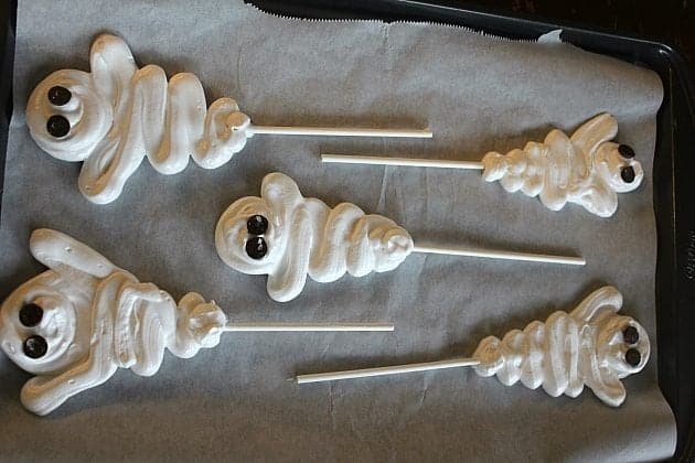 5 pieces ghosts shaped white Meringues on sticks with black eyes placed in parchment paper lined sheets