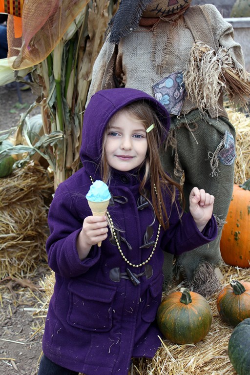 cute little girl holding her blue ice cream, standing near a scarecrow