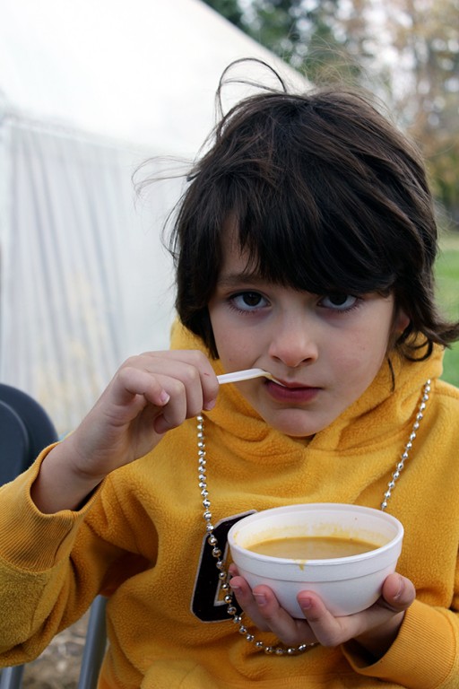 little boy wearing yellow jacket enjoying a bowl of soup