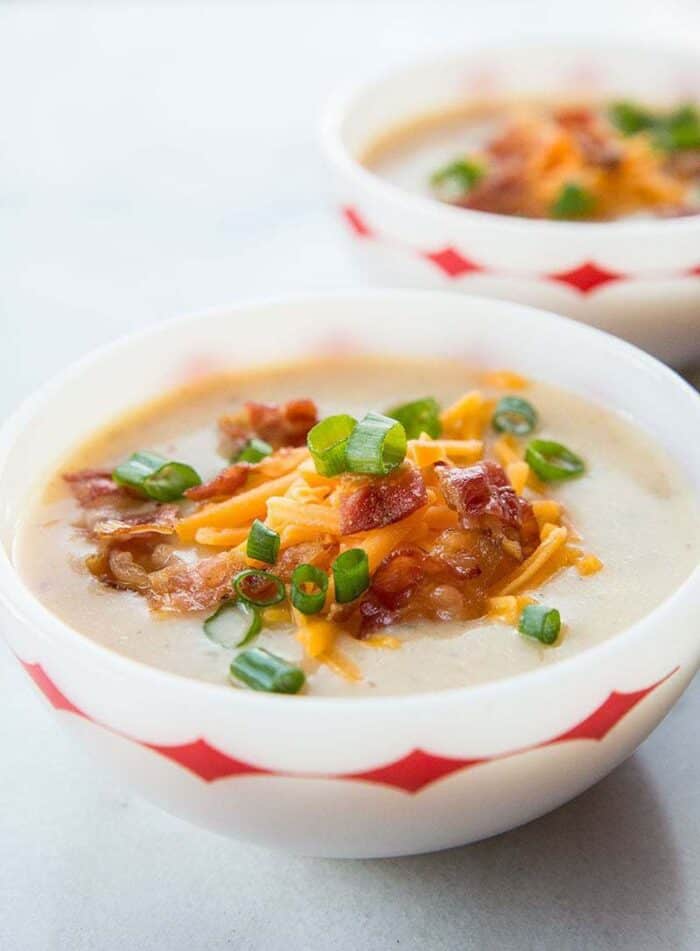 Close up of Two Bowls of Cheesy Bacon Potato Soup Served with Tex Mex Cheese, chopped green onions and extra bacon on top