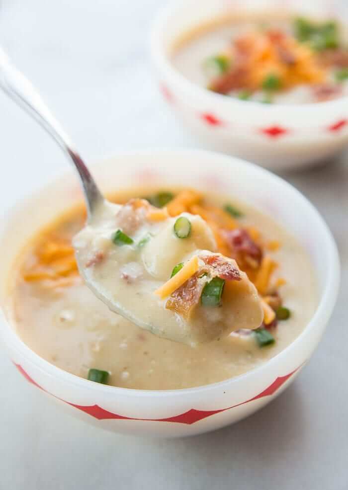 Spooning the Cheesy Bacon Potato Soup from a Red Diamonds FireKing Bowl