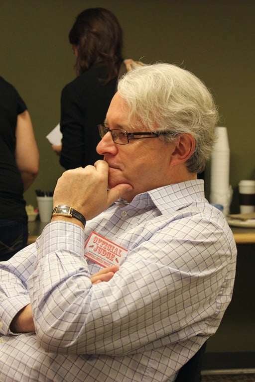 man with eye glasses and white hair, sitting while holding his chin