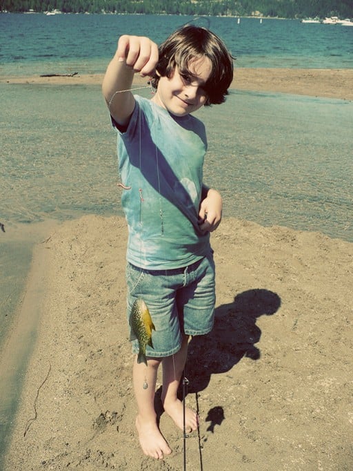 little boy near the lake water holding a string with a fish in it