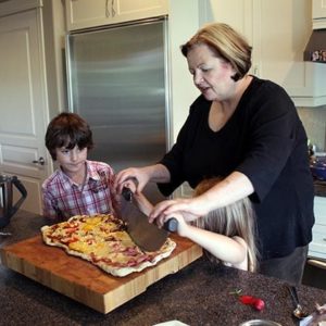woman helping the young little girl to slice the cooked pizza