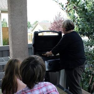 a woman cooking the pizza while two kids were sitting and watching her