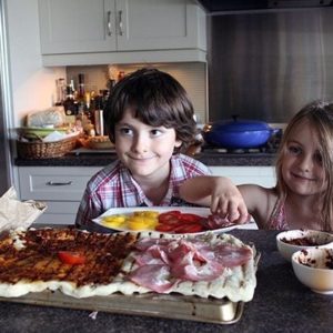 two kids adding the pizza sauce and toppings to the big dough