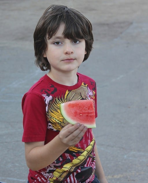 little boy wearing red shirt holding a slice of watermelon