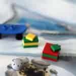 Small Lego pieces, including a blue skateboard, a gray helmet, and two stacked blocks—one red and one green/yellow—sit on a illustrated game board background resembling a snowy or icy landscape.