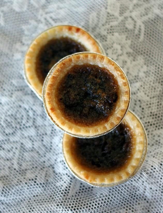 close up 3 pieces Butter Tarts with raisins on a white floral tablecloth background
