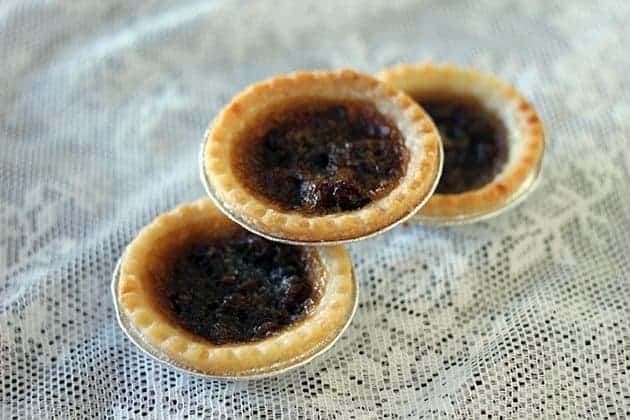 close up 3 pieces Butter Tarts with raisins on a white floral tablecloth background