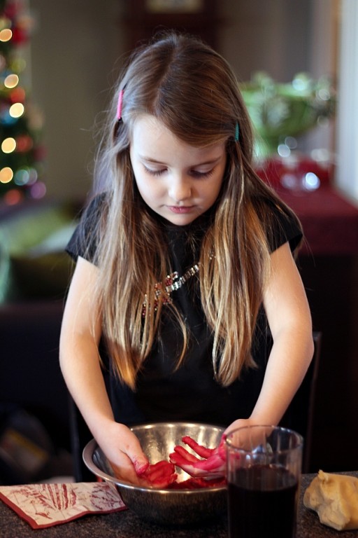 little girl with hands colored red inside the mixing bowl