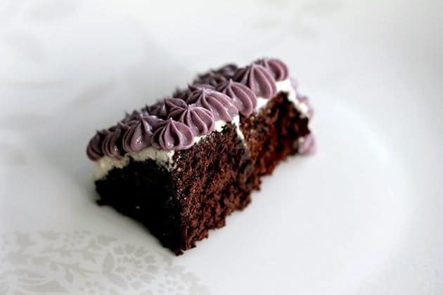 Gluten Free Chocolate Cake topped with violet vegan icing on white background