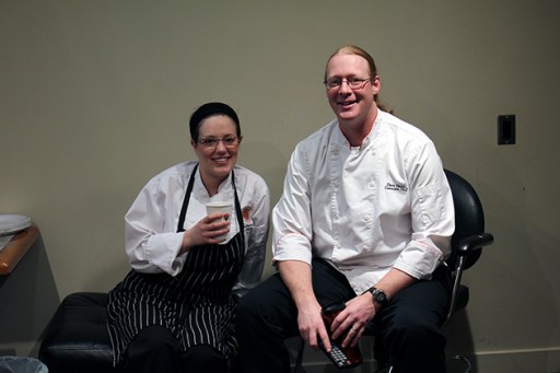 two chefs wearing white uniform, sitting and smiling for the photo