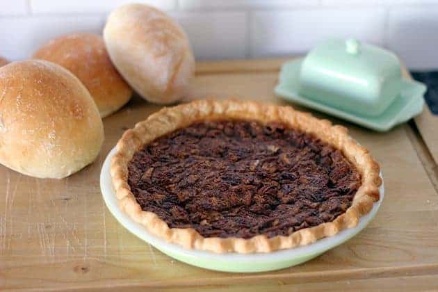 whole Quebec Maple Sugar pie in a pie plate, some pieces of buns on background