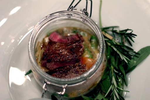 Jar with truffled beef on top of creamy vegetables served in a bowl of aromatic herbs