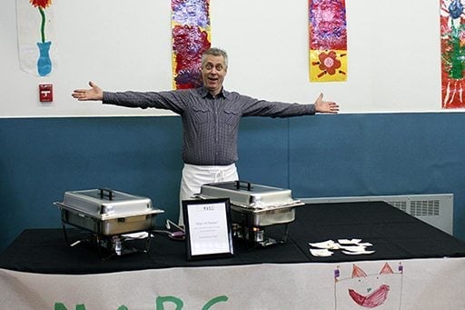 a chef standing beside the set up table with his both arms up on shoulder level