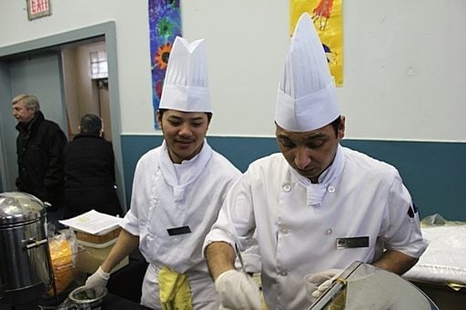 two chefs wearing white uniforms are busy in the kitchen