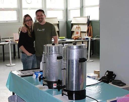 couple standing in the kitchen, two coffee dispensers on top of the table