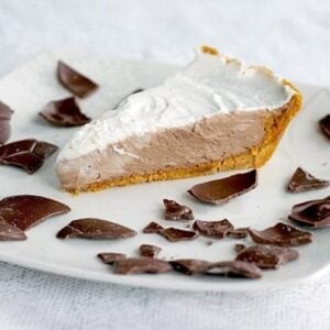 A slice of Chocolate Mousse Pie with whipping cream filling on top and crushed chocolate around a white plate