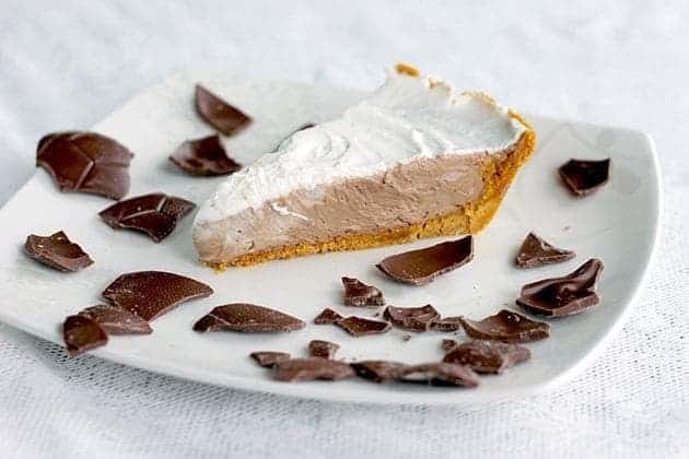 A slice of chocolate mousse pie in a white plate with crushed chocolates around the pie