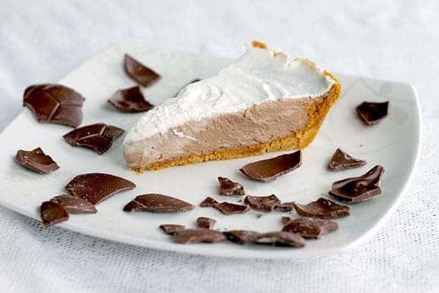 A slice of Chocolate Mousse Pie with whipping cream filling on top and crushed chocolate around a white plate