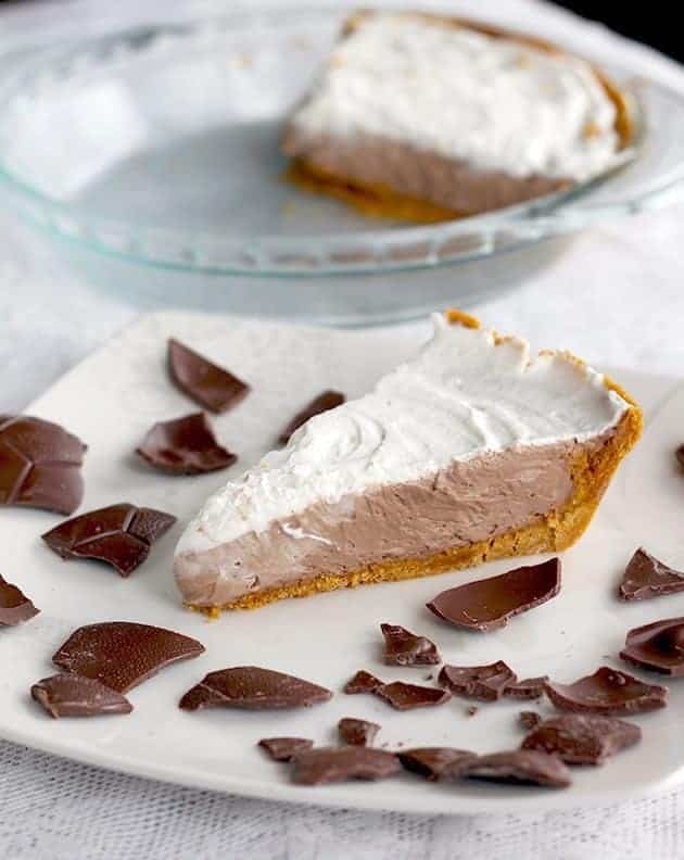 A slice of Chocolate Mousse Pie with whipping cream filling on top and crushed chocolate around a white plate