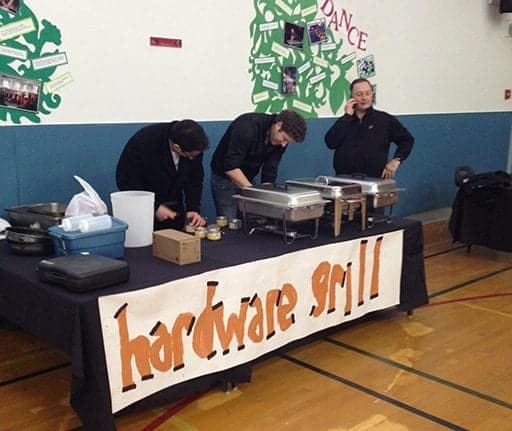 three man wearing black busy preparing foods at the hardware grill table