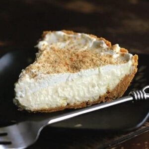 A slice of Lemon Cream Pie in a black plate with fork beside it