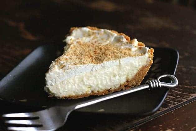 A slice of Lemon Cream Pie in a black plate with fork beside it