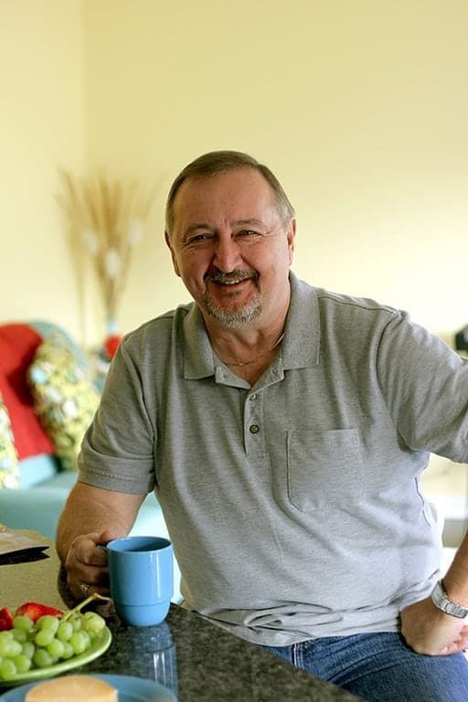 Handsome man wearing gray polo shirt sitting and holding a blue mug