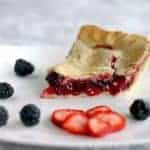 slice of strawberry pie in a white plate with some fresh strawberry slices and blackberries