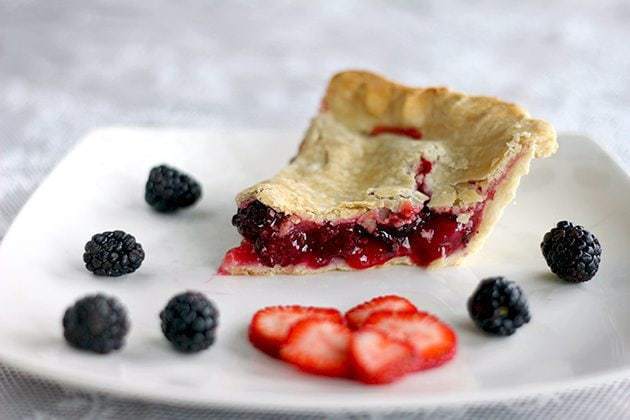 slice of strawberry blackberry pie with some fresh blackberries and slices of strawberries in a white plate