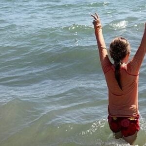 young girl in the sea water with two arms up