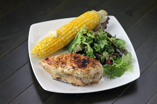 BBQ chicken breast in white plate with vegetable salad and corn in cob