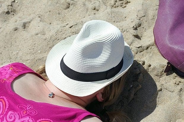 woman laying in the sand with face covered with cap