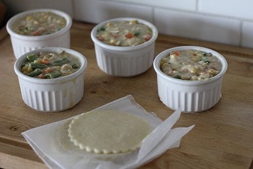 4 white ramekins filled with cooked chicken and vegetable soup, 4 pieces of cut out pie to cover each ramekins