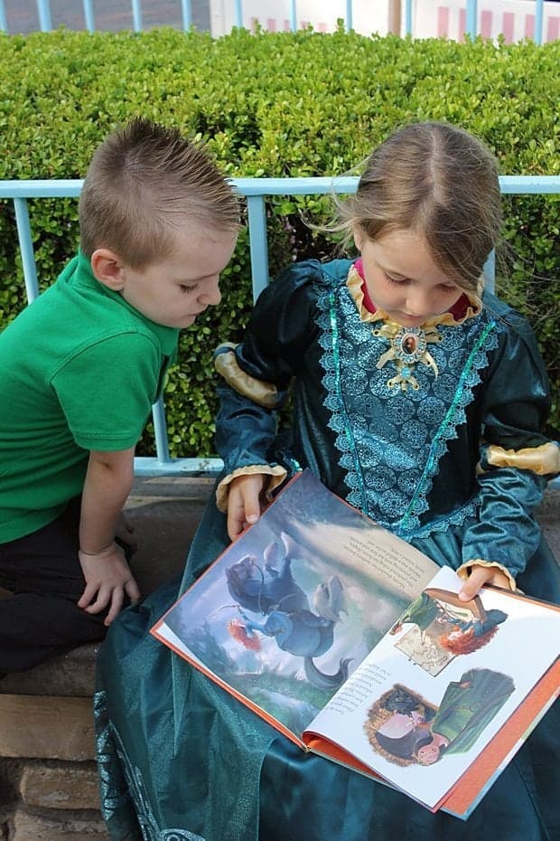 little girl reading the story of Princess Merida together with a little boy beside her