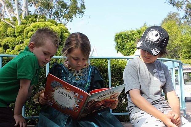 little girl reading the story of Princess Merida together with a little boy and older brother 