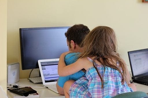 Dad in front of his laptop while his little daughter sitting on his back