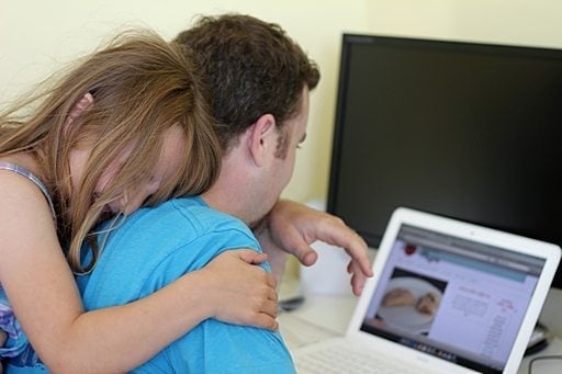 close up of little daughter sitting at the back of her Dad while in front of his laptop