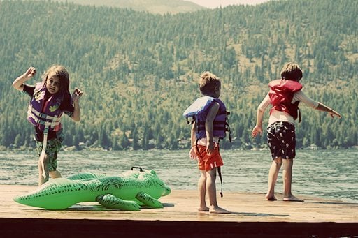 three kids wearing life jackets enjoying the lake
