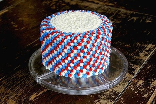 clear cake holder with Fourth of July cake with white, blue and red icing all over