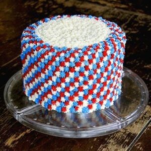 clear cake holder with Fourth of July cake with white, blue and red icing all over