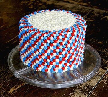 clear cake holder with Fourth of July cake with white, blue and red icing all over