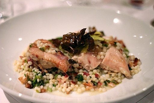 a plate of apple wood smoked chicken supreme with  bacon lardons, sautéed kale and Israeli couscous