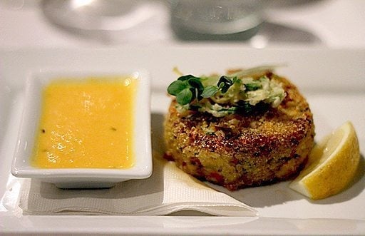 a serving of pacific crab cake with preserved lemon, fried leeks and burnt tangerine sauce.